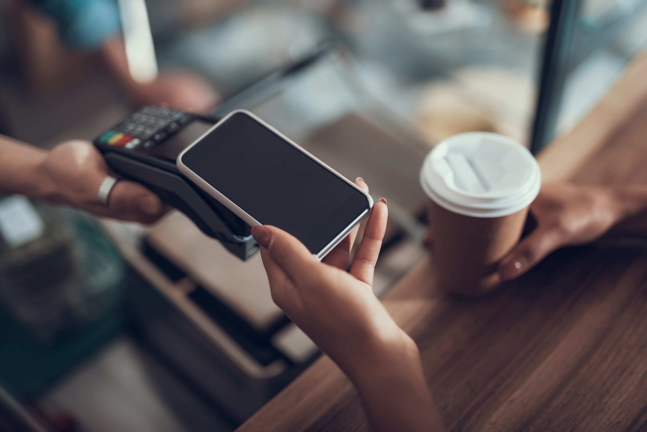 Des mains féminines tenant un smartphone au-dessus de la machine de paiement par carte de crédit tout en utilisant le système de paiement sans contact